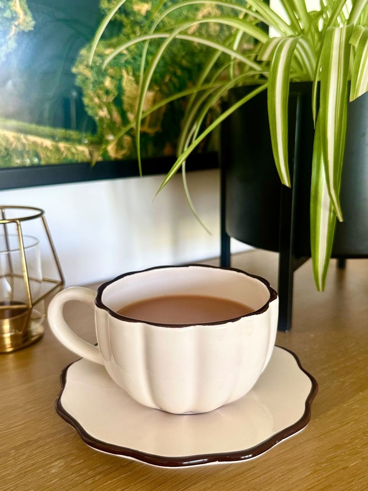 A cream cup of tea on a scalloped saucer beside a trailing spider plant.